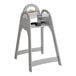 A gray unassembled high chair with a safety strap and a handle cutout on the backrest.