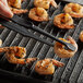 A person using Linden Sweden Gourmaid tongs to cook shrimp on a grill.