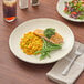 An Acopa ivory stoneware plate with salmon and vegetables on it, on a table with a glass of brown liquid.