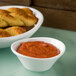 A white Carlisle melamine sauce cup filled with red sauce next to a plate of bread sticks.