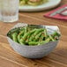 A round hammered stainless steel serving bowl filled with green beans.