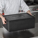 A chef holding a black Vollrath food pan carrier box with a square lid.