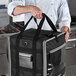 A person holding a black and grey Vollrath 5-Series delivery backpack bag.