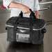 A person holding a large black Vollrath 3-Series food pan carrier bag.