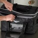 A person's hands opening a Vollrath medium insulated food pan carrier bag on a counter.