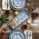 An American Metalcraft blue and white floral rectangular melamine tray set on a table with blue and white plates and bowls, a white spoon with white food in it, and a glass of red liquid.