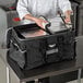 A chef putting food in a large black Vollrath food pan carrier bag.