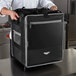 A man in a chef's uniform holding a large black Vollrath insulated tower bag.