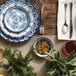 A table setting with American Metalcraft Isabella blue and white melamine bowls and plates with a glass of red liquid and a plant.