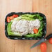 A black Cambro deli crock filled with salad on a wooden surface next to a knife.