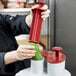 A woman using a Robot Coupe R2N food processor to slice a cucumber on a counter.