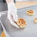 A person in white gloves holding a cinnamon roll on a Chicago Metallic wire in rim aluminum sheet.