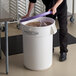 A person holding a purple lid over a white Baker's Lane ingredient storage bin full of brown grains.