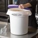 A woman using a purple lid to close a Baker's Lane white ingredient storage bin.