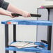 A person holding a laptop over a blue Luxor utility cart shelf.