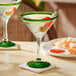 An Acopa martini glass with a green rim and base filled with a green drink and olives.