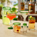 A variety of Acopa Tropic glass pitchers with green rims filled with different colored drinks on a table.