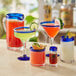 An Acopa glass pitcher with a blue rim on a table with glasses and drinks.