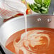 Unsweetened coconut milk being poured into a pot of soup.