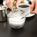 A person pouring sugar into an Anchor Hocking glass container with a spoon.