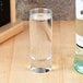 A Libbey cordial glass filled with clear liquid next to a bottle of clear liquid.