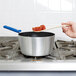 A person stirring food in a Vollrath Wear-Ever sauce pan with a blue silicone handle.