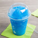 A clear plastic squat dome lid with a blue straw in a plastic cup with a blue slushy.