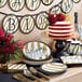 A stack of black and gold "Happy Birthday" dinner napkins on a table with plates and a cake.