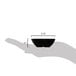 A hand holding a small black Carlisle square ramekin.