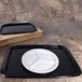 A black rectangular bamboo tray with a white plate on it.