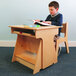 A young boy reading a book at a Whitney Brothers standing children's desk.