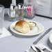 A Tuxton ivory china plate with an embossed rim on a table with a roll and utensils.