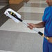 A man in blue scrubs holding a Rubbermaid HYGEN white microfiber mop pad on a yellow and black handle.