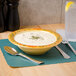 A Venetian melamine bowl of soup with a spoon next to a fork on a green surface.