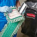 A person in blue scrubs holding a green and white Rubbermaid microfiber fringed dust mop pad.