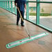 A man in a blue uniform using a Rubbermaid green microfiber fringed dust mop to clean the floor.