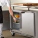 A man in a white shirt and black pants opening a Beverage-Air undercounter refrigerator on a counter.