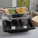 A person pouring water into a clear plastic container of food.