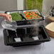A person pouring water into a black Sterno SpeedHeat container on a table in an outdoor catering setup.