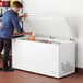 A man opening a Galaxy commercial chest freezer filled with food.