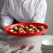 A person holding a red HS Inc. plastic serving tray with food on it.