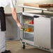 A man in a chef's uniform putting a glass bottle of food into a Beverage-Air undercounter refrigerator.