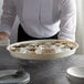 A waiter holding a white round plastic serving tray of oysters on ice.