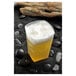 A Fineline clear plastic tumbler filled with beer and foam on black rocks.