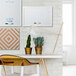 A MasterVision white dry erase board on a white wall above a white desk and chair.