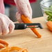 A black-handled OXO Good Grips 7-inch straight vegetable peeler being used to peel a carrot on a wooden cutting board.
