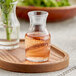 A Libbey glass cocktail decanter filled with pink liquid on a wooden tray.