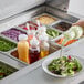 A clear polycarbonate bottle of salad dressing being filled at a salad bar.