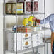 A man putting a yellow bottle of vegetable oil on a Regency chrome wire shelf full of food.