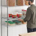 A man standing in front of a Regency chrome wire shelf with food containers.